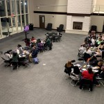 Students are seated at 6 round tables in the Great Hall at the Ferguson Center with two screens positioned at the front of the room displaying questions