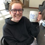 A smiling person with glasses proudly displays a decorated mug